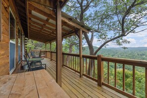 A wooden deck with a table and chairs, overlooking a forested landscape.
