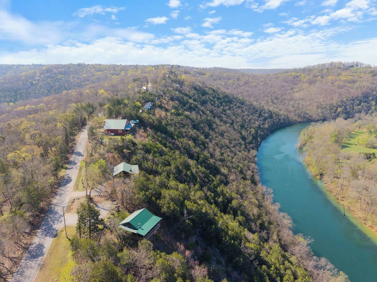 A river winding through a forested area with a few buildings along a dirt path.