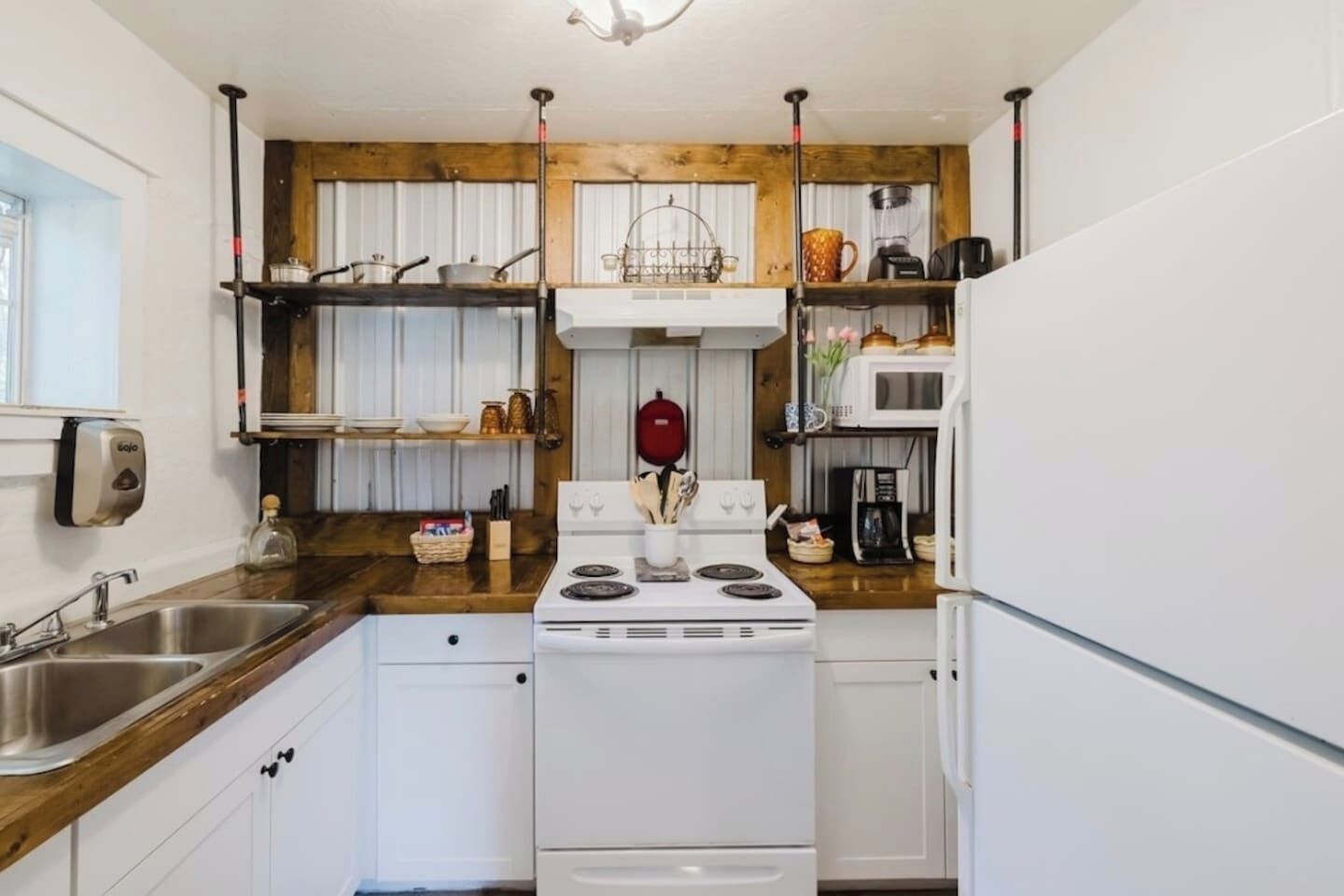 Une cuisine de taille réduite, dotée d’appareils électroménagers blancs, de plans de travail en bois et d’un îlot central.