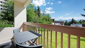 Een balkon met een tafel en stoelen, een houten hekwerk en uitzicht op bergen en bomen.