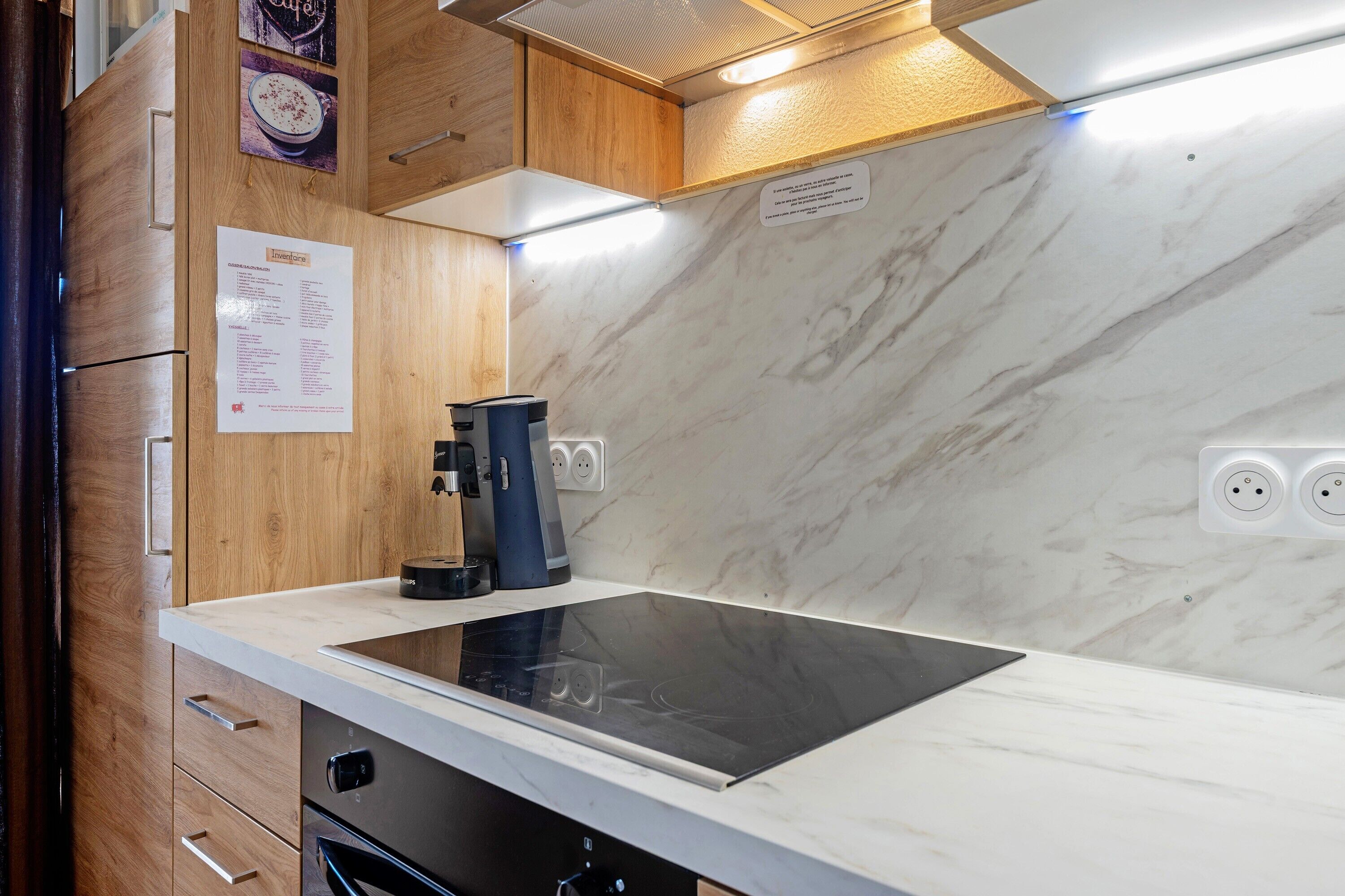 Une cuisine moderne dotée d’une plaque de cuisson à induction intégrée, de meubles en bois et d’un dosseret en marbre.
