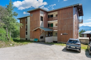 Un bâtiment à deux étages avec une façade en bois, un balcon et une voiture garée devant.