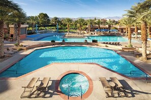 A large outdoor swimming pool with multiple sections, surrounded by palm trees and lounge chairs. - Coachella Weekend 2 - Shadow Ridge Village 1 Condo (Palm Desert)
