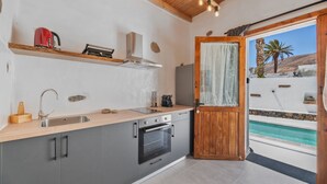 Una cucina moderna con piano di lavoro in legno, elettrodomestici in acciaio inossidabile e vista su una piscina attraverso una porta aperta.