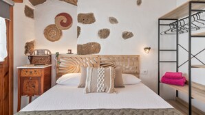Una camera da letto con un letto, una testiera in legno, decorazioni murali in pietra, un comodino in legno e una mensola metallica con asciugamani.