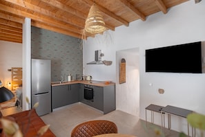 Een compacte keuken met moderne apparaten, een eethoek met een comfortabele stoel en een flatscreen televisie aan de muur.
