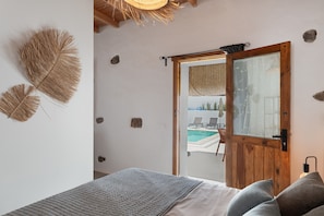Een slaapkamer met een bed, een houten deur naar een zwembadgedeelte en decoratieve wandelementen.