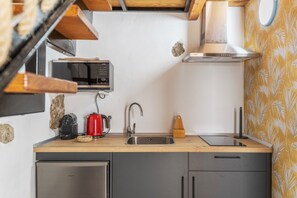 Una cocina compacta equipada con microondas, hervidor de agua, pileta y un refrigerador pequeño.