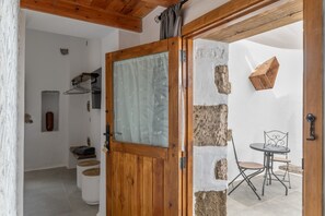 Una puerta de madera con un panel de vidrio, una pared de piedra, una mesa pequeña con sillas y un perchero colgado.