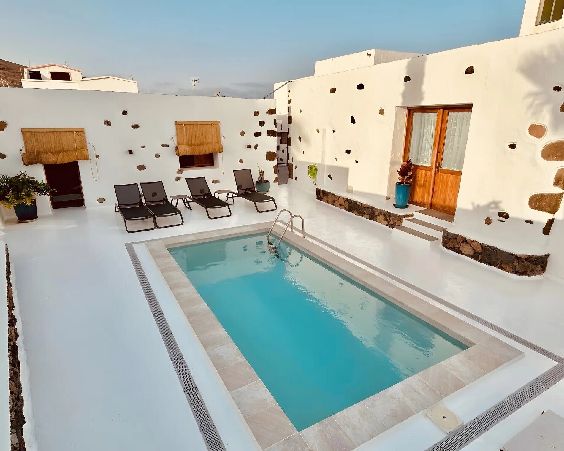 Una piscina con sillones de descanso, una puerta de madera y un muro de piedra.