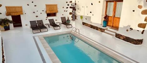 Una piscina con sillones de descanso, una puerta de madera y un muro de piedra.