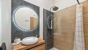 Een moderne badkamer met een ronde spiegel, een witte wasbak, een houten opbergmeubel, een douche met glazen wanden en een houten douchegordijn.
