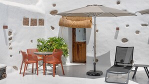 Een terras met witte wanden, een ronde tafel, oranje stoelen, een grote parasol en een lounge stoel.