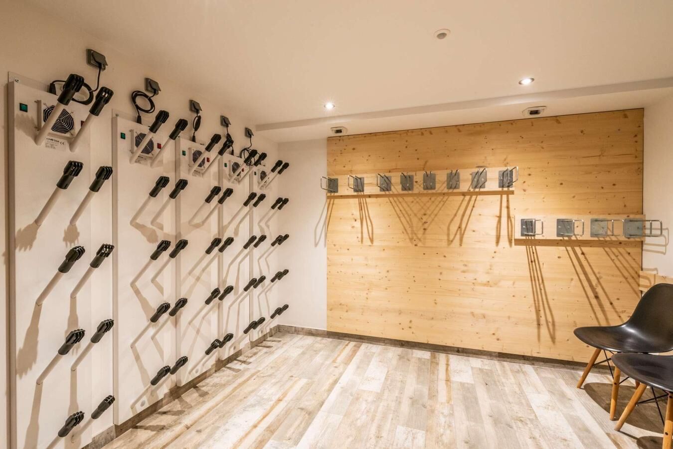 Ein Zimmer mit einem an der Wand befestigten Gestell schwarzer Gegenstände, einer Holzpaneelwand und einem schwarzen Stuhl.