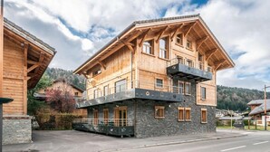A multi-story wooden building with balconies, stone foundation, and a mountainous backdrop. - Up to 250 meters from the gondola lifts, ground floor, fitness center, hammam, terrace, TV (Morzine)