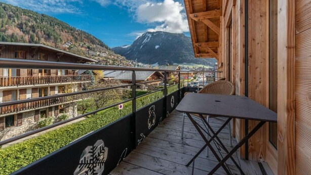 A wooden balcony with a table and chairs, overlooking a mountainous landscape with buildings and a clear sky. - Up to 250 meters from the gondola lifts, ground floor, fitness center, hammam, terrace, TV (Morzine)