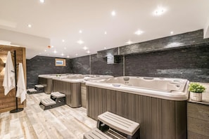 A modern bathroom with three large tubs, wooden flooring, and a dark brick wall. - 50m to city center, first floor, fitness, hammam, terrace, tv (Morzine)
