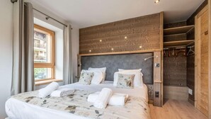 A modern bedroom with a large bed, wooden headboard, and a built-in wardrobe. - Up to 250 meters from the gondola lifts, ground floor, fitness center, hammam, terrace, TV (Morzine)