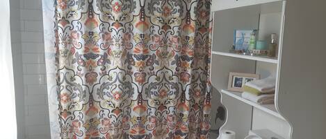A bathroom with a shower curtain featuring a floral pattern, a toilet, and a shelf with toiletries.