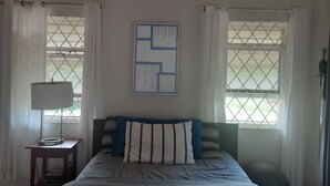 A bedroom with a bed, a nightstand, a lamp, and a window with curtains. -  A Hidden Bed & breakfast with live-in host  Private, Peaceful with Plunge pool. (Christ Church)