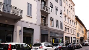 Reihung geparkter Autos an einer Kopfsteinpflasterstraße, gesäumt von mehrstöckigen Gebäuden mit Balkonen und Geschäften.