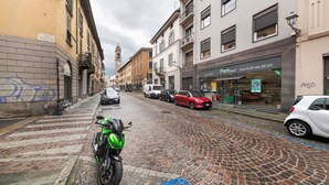 A cobblestone street with buildings, a motorcycle, and parked cars. - Room 'Enza 1' with Wi-Fi (Bergamo)