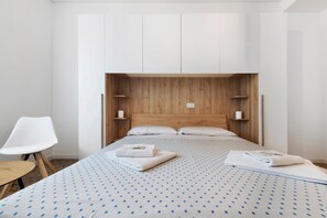 A bedroom with a bed, white chair, wooden headboard, and a small shelf.
