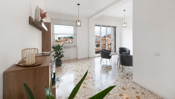 A spacious living area with a large window, a wooden console table, a potted plant, and a black chair. - Room 'Enza 1' with Wi-Fi (Bergamo)