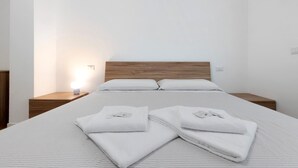 Un lit bien fait, avec du linge de lit et des serviettes blanches, une tête de lit en bois et une table de chevet avec une lampe.