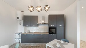 Une cuisine moderne avec des armoires grises, un four encastré, une cuisinière à gaz et un chauffe-eau. On y trouve une table à manger avec deux chaises et une tasse posée dessus.
