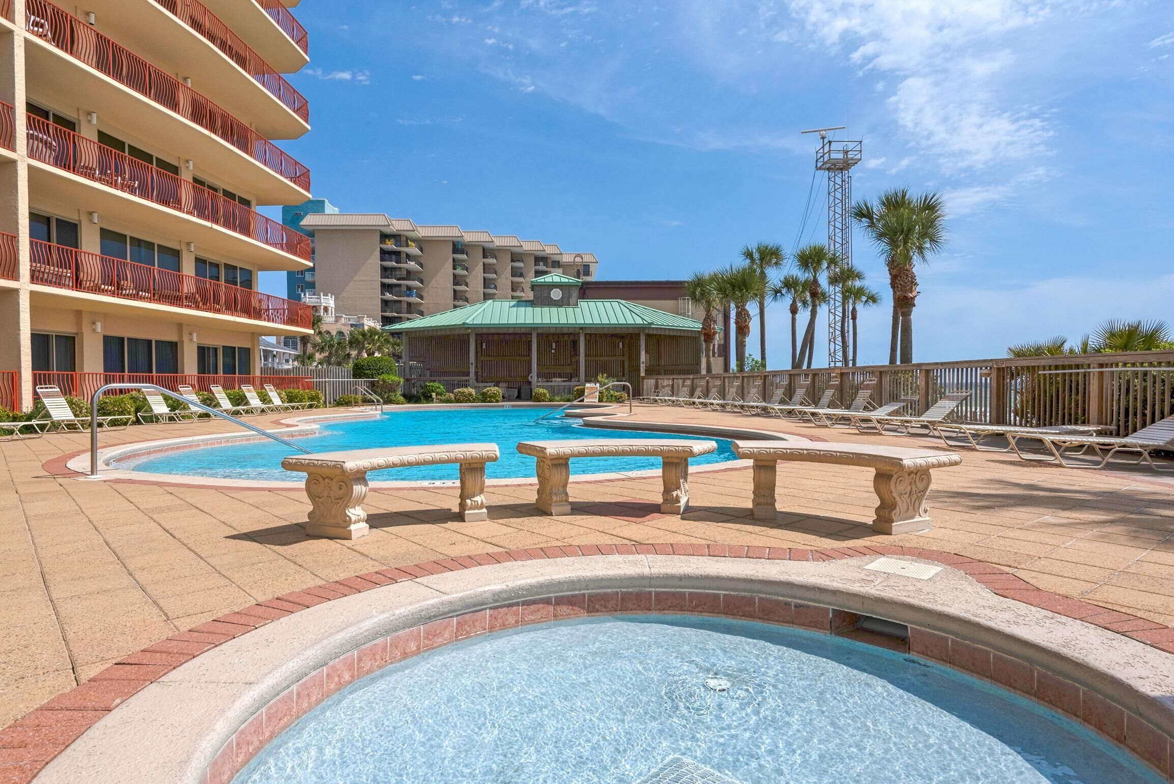A hotel pool area with lounge chairs, a hot tub, and a view of the hotel buildings.