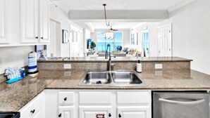 A modern kitchen with white cabinetry, granite countertops, and a stainless steel sink. - Tropic Winds 503 (Panama City Beach)