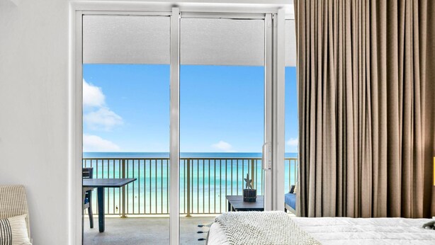 A hotel room with a large sliding glass door leading to a balcony with a view of the ocean. - Tropic Winds 503 (Panama City Beach)