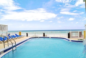 A swimming pool with a view of the ocean, blue lounge chairs, and a white fence. - Tropic Winds 503 (Panama City Beach)