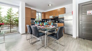 A modern kitchen with wooden cabinets, stainless steel appliances, and a glass dining table with chairs. - Blue Pelagos Villa - Three Bedroom Villa, Sleeps 6 (Pernera)