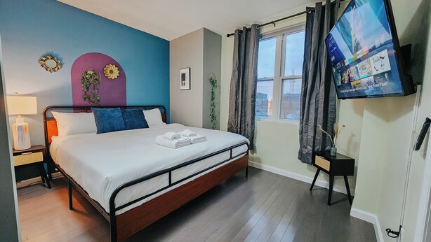 A neatly arranged bedroom with a bed, bedside table, lamp, and a TV mounted on the wall.