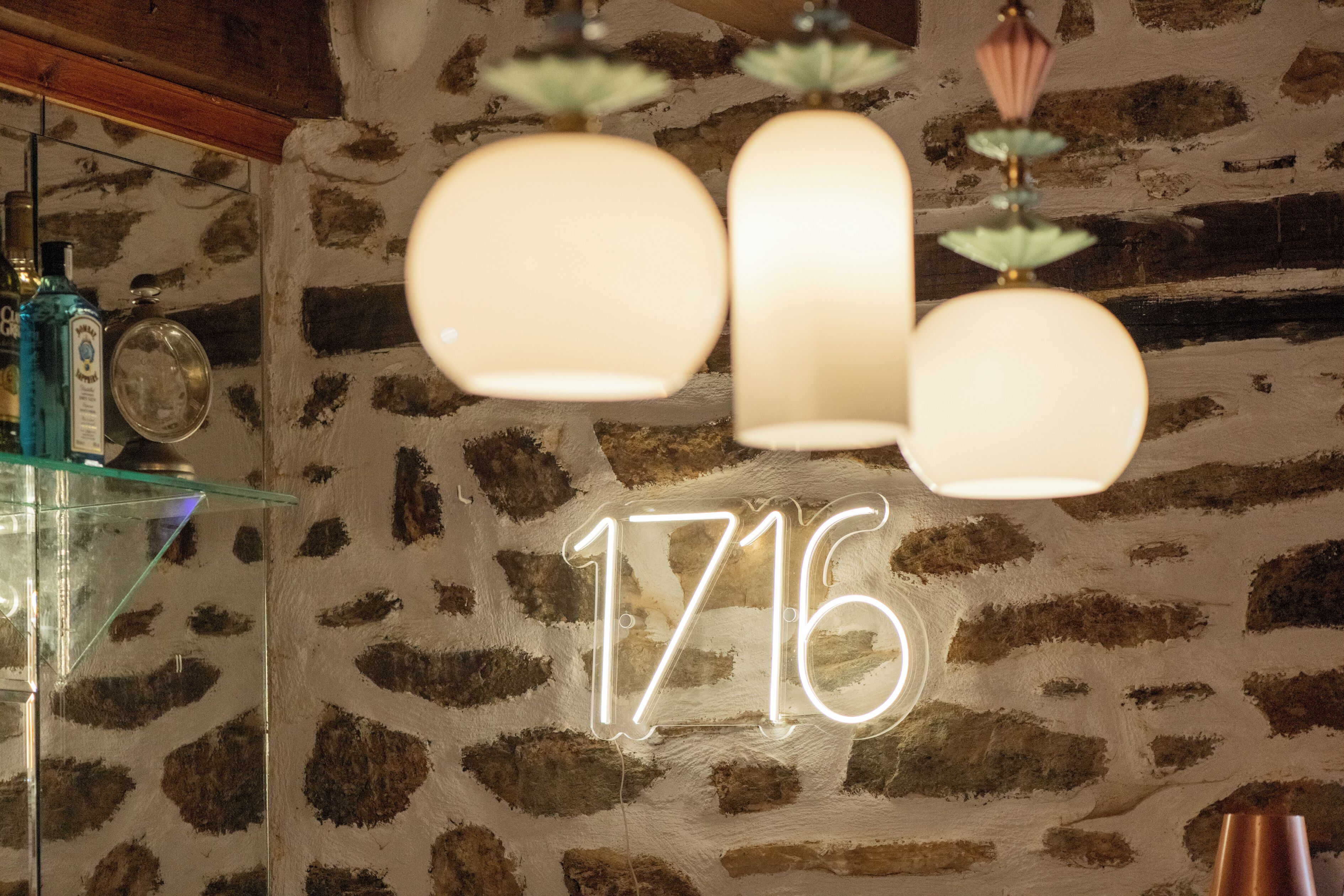 En stenvæg med et neonskilt der viser "1716" og hængende lysekroner.