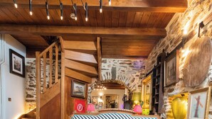 A cozy living room with a striped sofa, a wooden staircase, and rustic stone walls. - Archontiko 1716 (Volos)