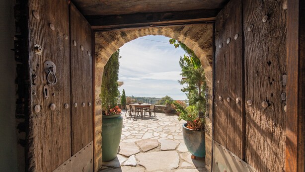 An arched stone pathway leading to a patio with outdoor furniture and potted plants. - Archontiko 1716 (Volos)