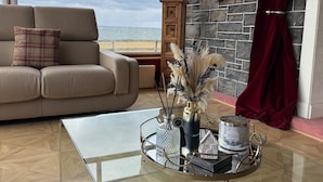 A living room with a beige sofa, a glass coffee table, a decorative tray with items, a view of the beach, and a stone wall. - Strathlene House Retreat - 5 Bedrooms (Buckie)
