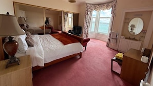 A hotel room with a large bed, a desk, a chair, a mirror, and a view of the sea. - Strathlene House Retreat - 5 Bedrooms (Buckie)