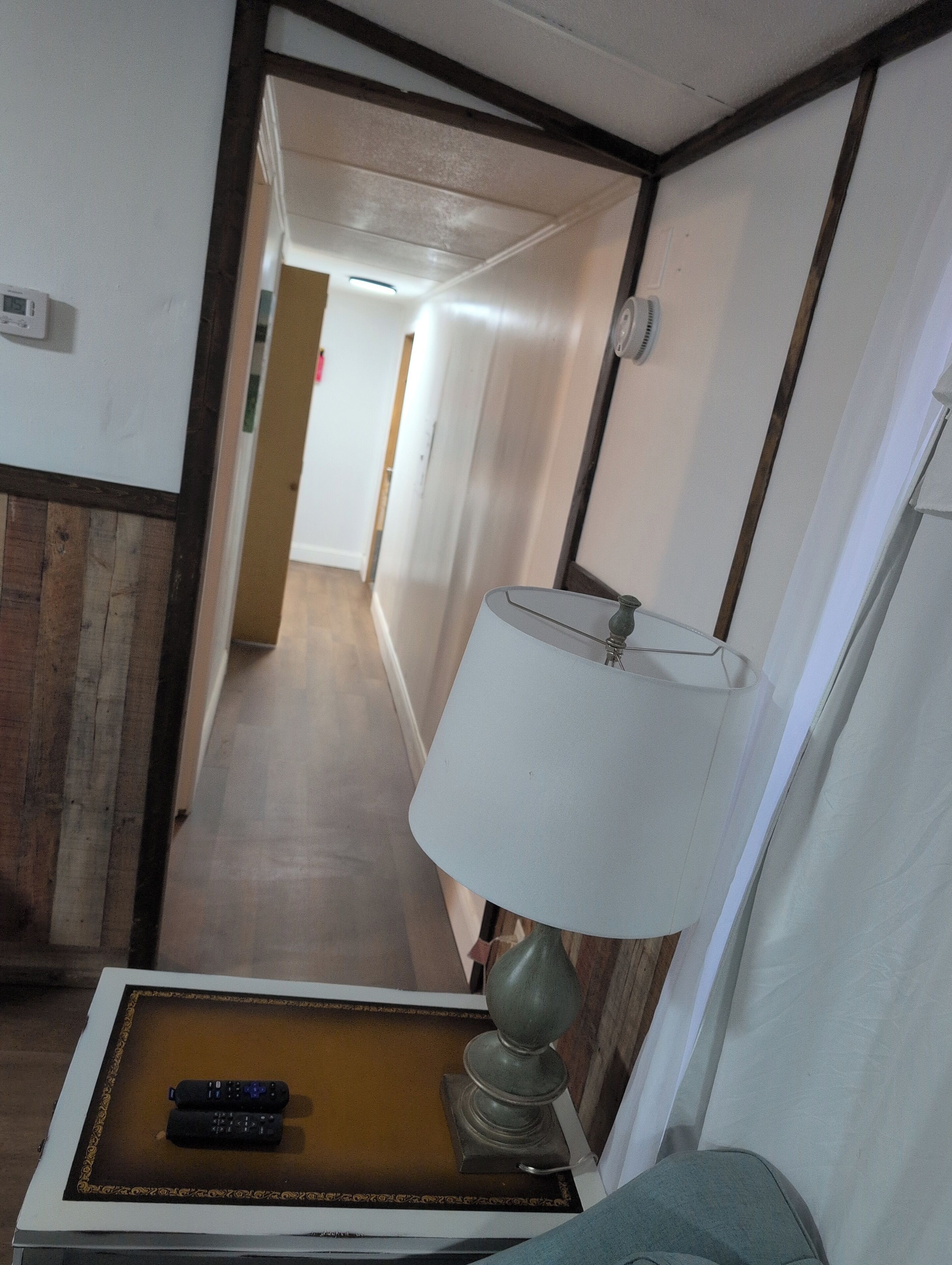 A hotel hallway with a lamp, a remote control on a tray, and a wooden floor.