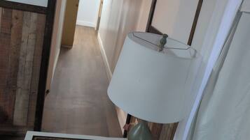 A hotel hallway with a lamp, a remote control on a tray, and a wooden floor.