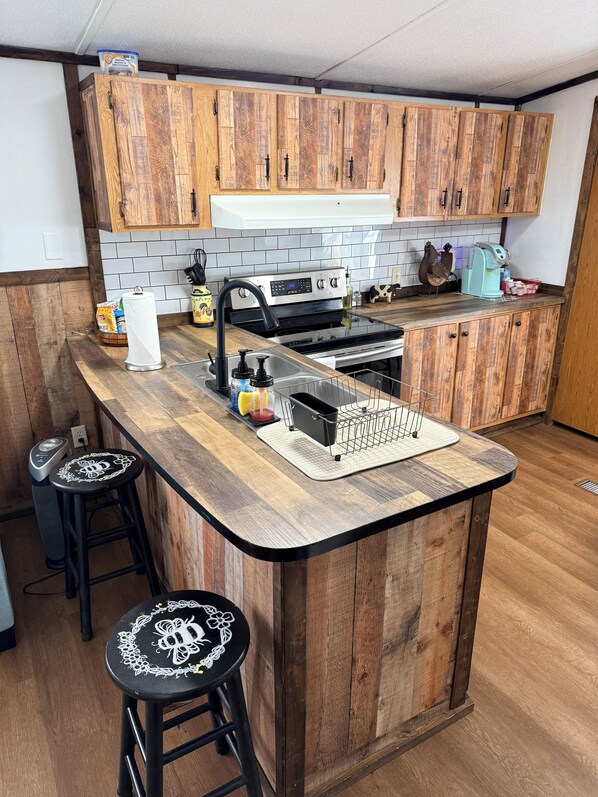 A kitchen with wooden cabinets, a stainless steel stove, and a bar area with stools. - Farmhouse mobile home with Wi-Fi, AC in lovely Dayton (Dayton)