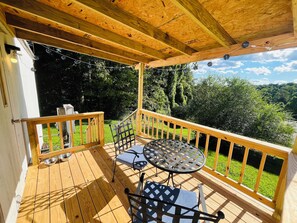 Une terrasse en bois, agrémentée d’une table et de chaises, entourée d’une balustrade et offrant une vue sur un paysage verdoyant et luxuriant.