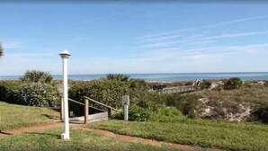 Un sendero costero que lleva a un faro blanco, rodeado de vegetación y con una vista despejada del mar.