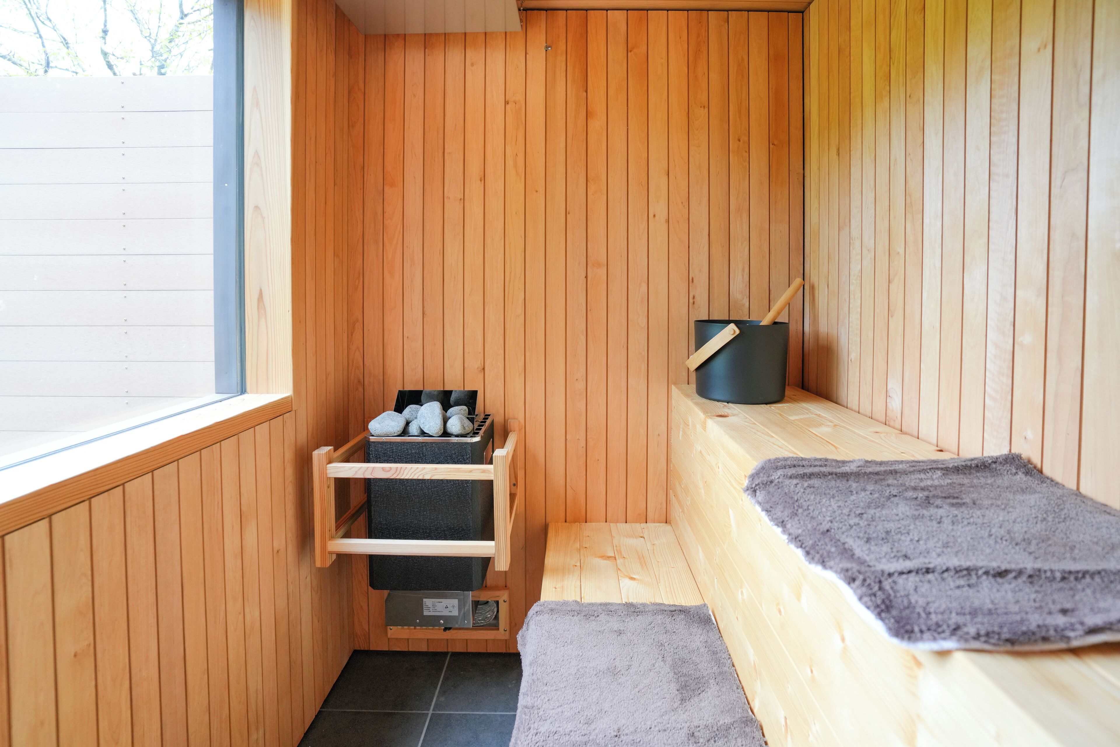 Uma sauna de madeira com um banco, uma prateleira com pedras e um recipiente preto.