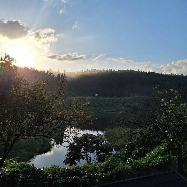 A serene landscape with a lake, forested hills, and a tent in the distance. - Sakata Log House (Sakata)