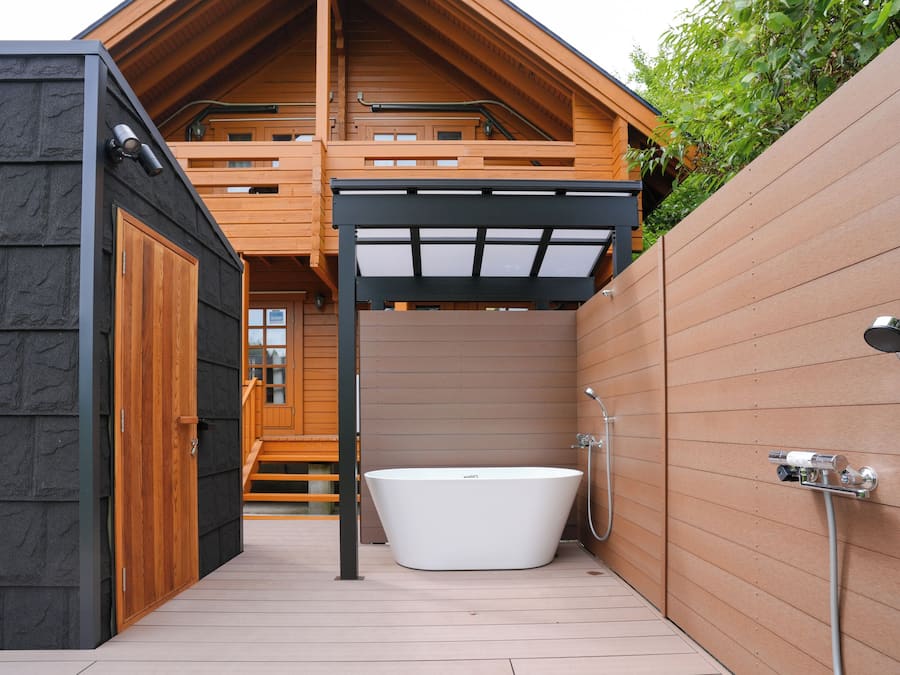 Una cabaña de madera con un porche de madera, una bañera blanca y una cerca de madera.