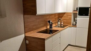 Een kleine keuken met witte kastjes, een houten aanrechtblad en een inbouwmagnetron.